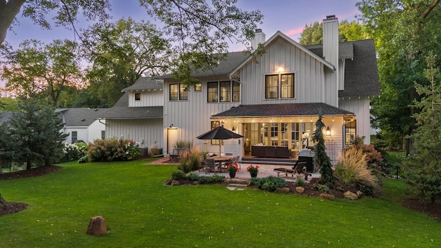back of property at dusk with board and batten siding, a patio area, a yard, and a chimney