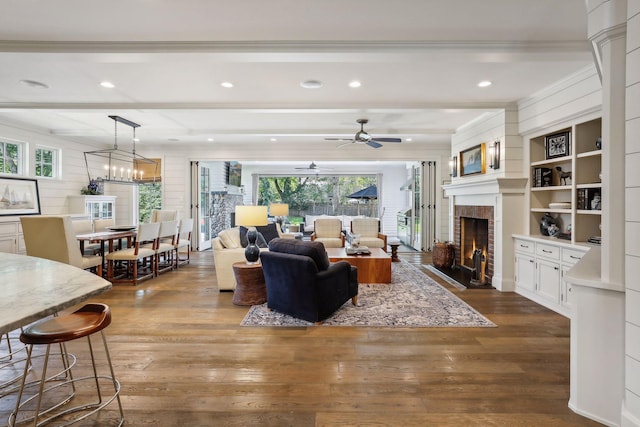 living area featuring ornamental molding, a brick fireplace, beam ceiling, dark wood-type flooring, and a ceiling fan