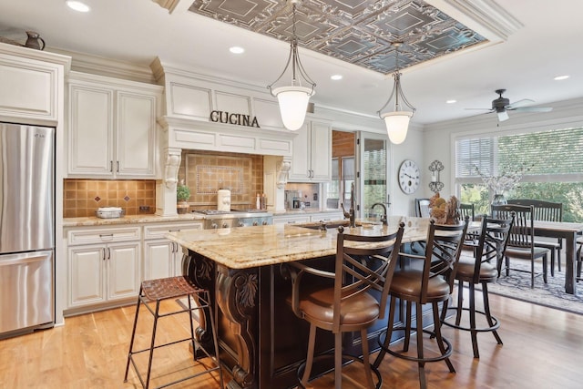 kitchen with stainless steel refrigerator, decorative light fixtures, a breakfast bar, an island with sink, and light stone counters