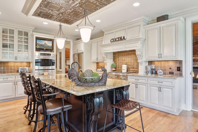 kitchen with stainless steel appliances, an island with sink, white cabinetry, and light hardwood / wood-style flooring