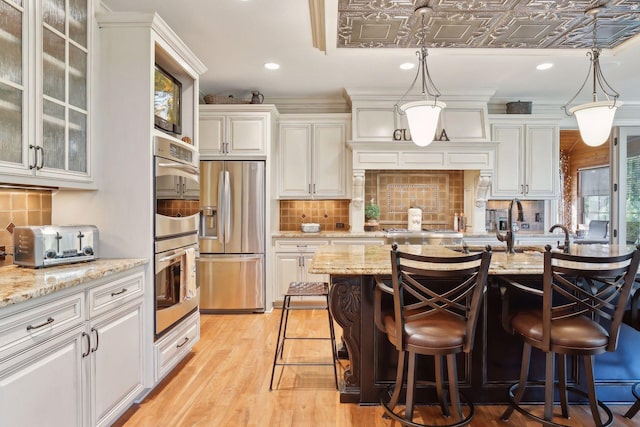 kitchen featuring light stone countertops, appliances with stainless steel finishes, white cabinets, a breakfast bar, and backsplash