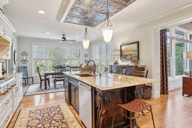 kitchen featuring dishwasher, white cabinetry, a kitchen island with sink, sink, and pendant lighting