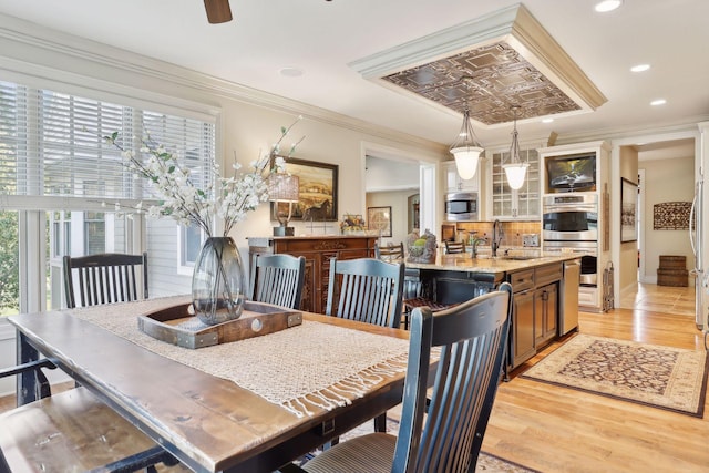 dining room featuring sink, ceiling fan, a tray ceiling, light hardwood / wood-style flooring, and crown molding