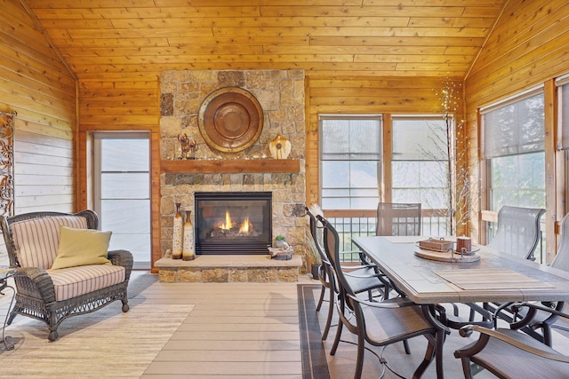 dining area featuring wood-type flooring, a fireplace, wooden ceiling, high vaulted ceiling, and wooden walls