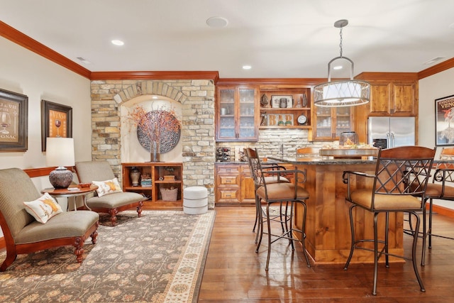 interior space featuring a kitchen bar, stainless steel fridge with ice dispenser, hardwood / wood-style flooring, hanging light fixtures, and ornamental molding