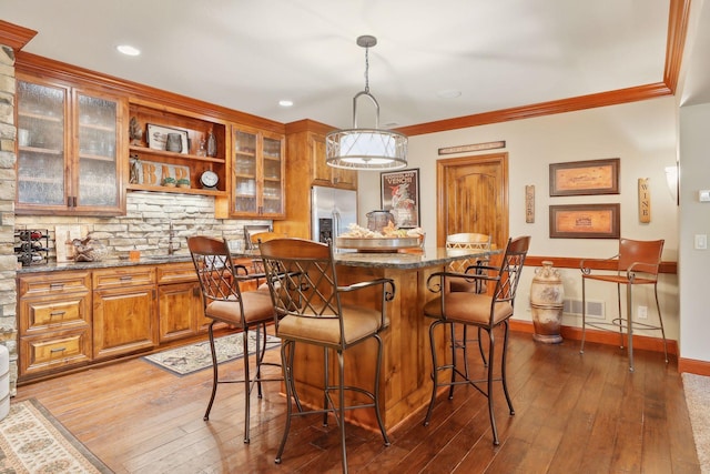 kitchen featuring light hardwood / wood-style floors, stainless steel fridge with ice dispenser, ornamental molding, pendant lighting, and dark stone counters