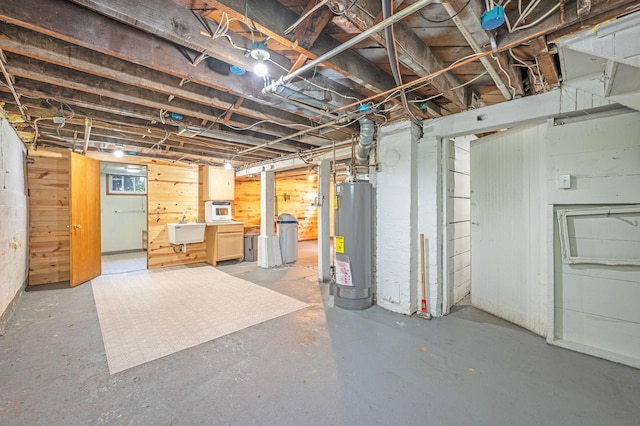 basement featuring water heater, sink, and wood walls