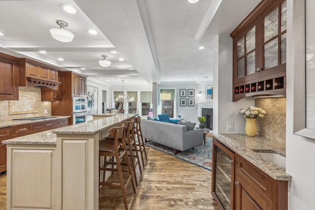 kitchen with light stone counters, wine cooler, tasteful backsplash, a center island, and light hardwood / wood-style flooring