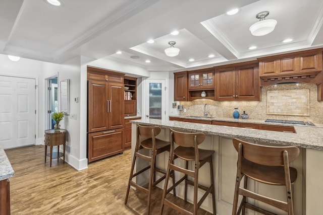 kitchen with light stone counters, a breakfast bar area, paneled built in fridge, light hardwood / wood-style flooring, and decorative backsplash