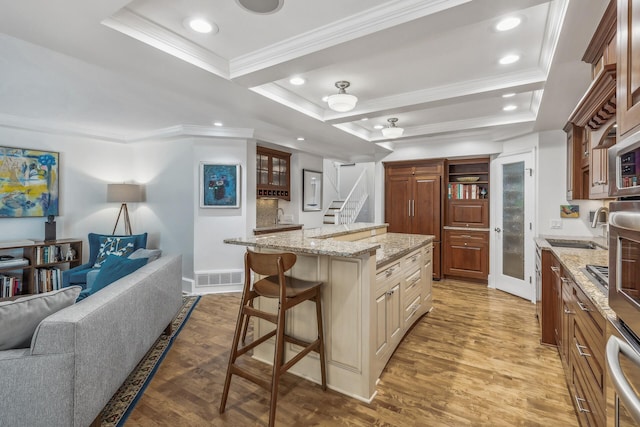 kitchen featuring dark wood-type flooring, light stone counters, a kitchen island, a breakfast bar area, and crown molding