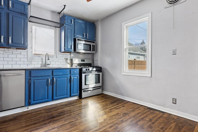 kitchen with appliances with stainless steel finishes, tasteful backsplash, sink, light stone counters, and blue cabinetry