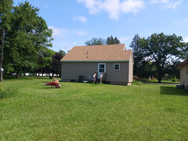 back of house with entry steps, a yard, and roof with shingles