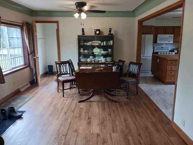 dining area featuring baseboards, baseboard heating, a ceiling fan, and light wood finished floors