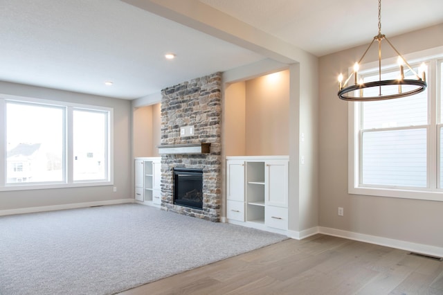 unfurnished living room featuring a stone fireplace, a notable chandelier, and light wood-type flooring