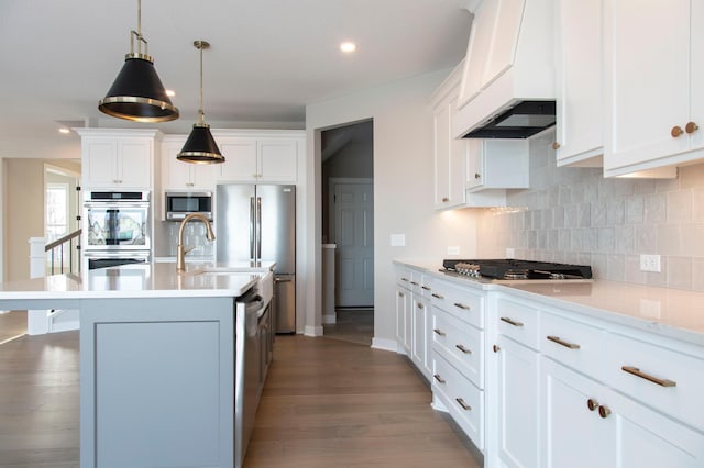 kitchen featuring white cabinetry, hanging light fixtures, a center island with sink, stainless steel appliances, and decorative backsplash