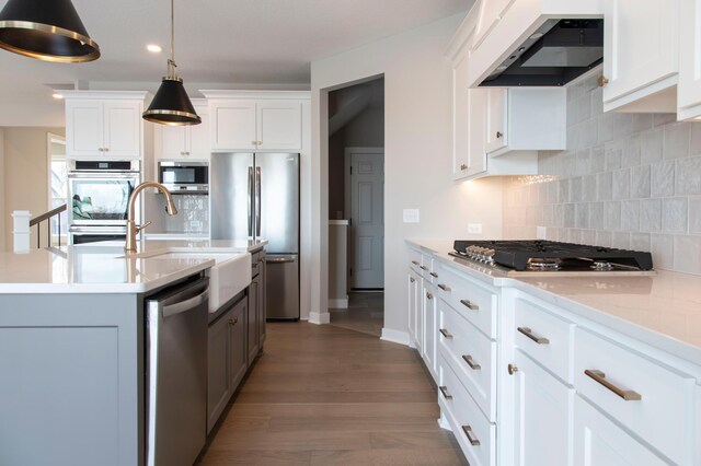 kitchen with appliances with stainless steel finishes, white cabinetry, sink, hanging light fixtures, and wall chimney exhaust hood