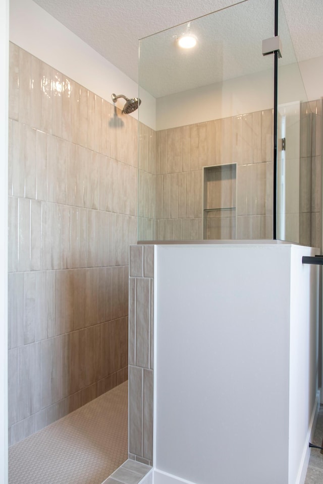 bathroom with a textured ceiling and a tile shower