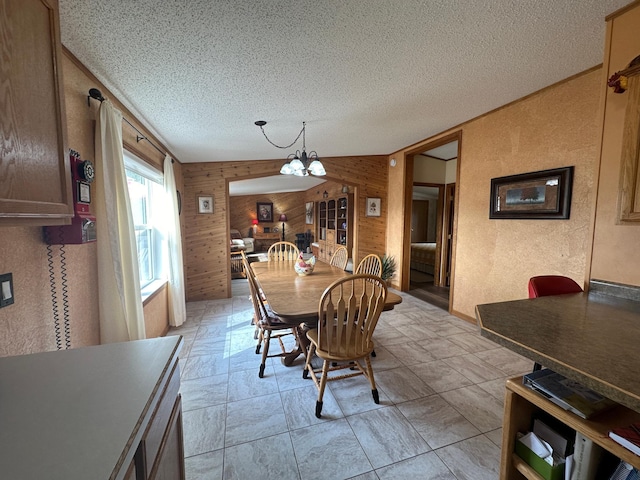 dining room featuring lofted ceiling, a chandelier, wooden walls, and a textured ceiling