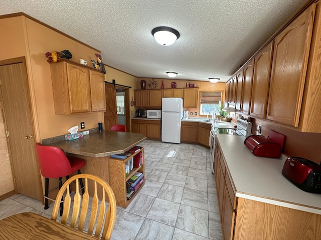 kitchen featuring a textured ceiling, brown cabinetry, white appliances, a sink, and a peninsula