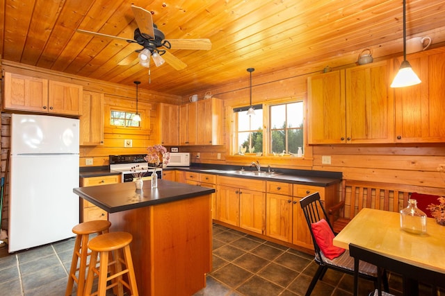 kitchen with wooden walls, white appliances, a kitchen island, sink, and ceiling fan