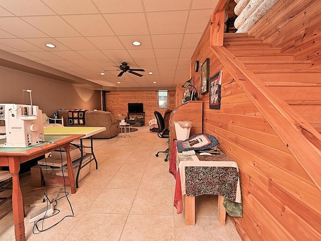 interior space featuring a wood stove, ceiling fan, light tile patterned flooring, and a drop ceiling