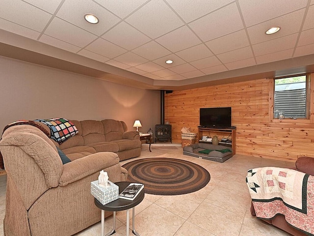 living room with a wood stove, a paneled ceiling, wooden walls, and tile patterned floors