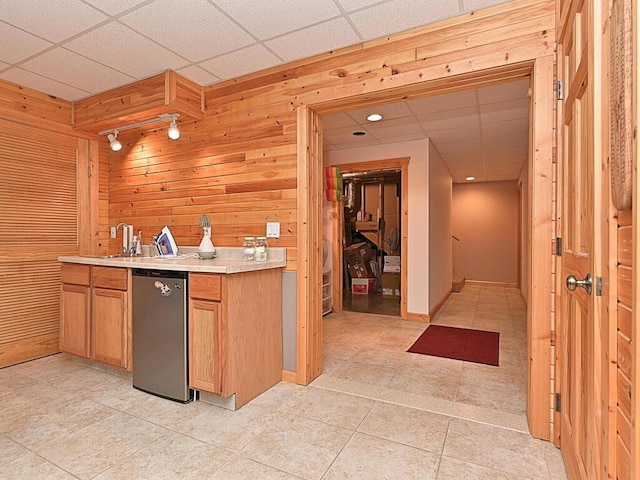 kitchen with light tile patterned flooring, sink, wooden walls, and a drop ceiling