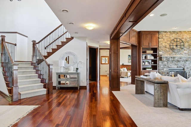 living room with dark wood-style flooring, a stone fireplace, stairs, and baseboards