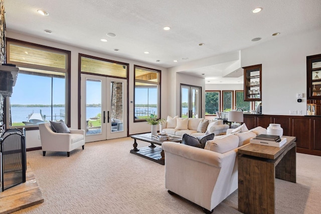 living area featuring french doors, light carpet, recessed lighting, a water view, and a textured ceiling