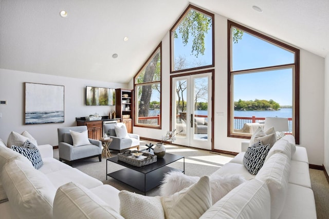 living area with light colored carpet, high vaulted ceiling, baseboards, and a water view