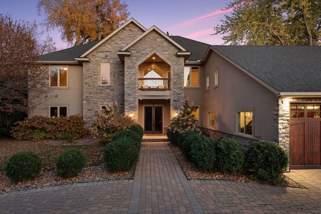 view of front facade featuring french doors, a balcony, and stone siding