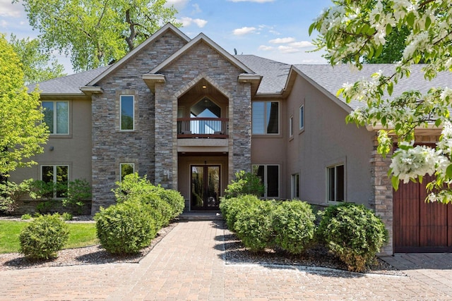 traditional home featuring a balcony, french doors, stucco siding, and stone siding