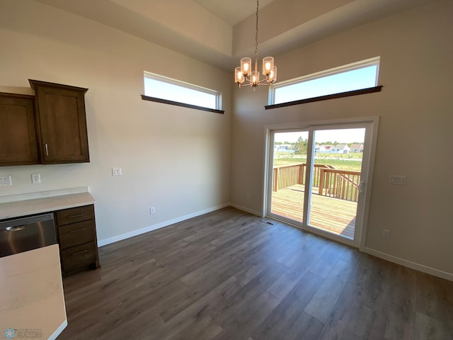 unfurnished dining area featuring a chandelier, baseboards, a high ceiling, and dark wood-style floors