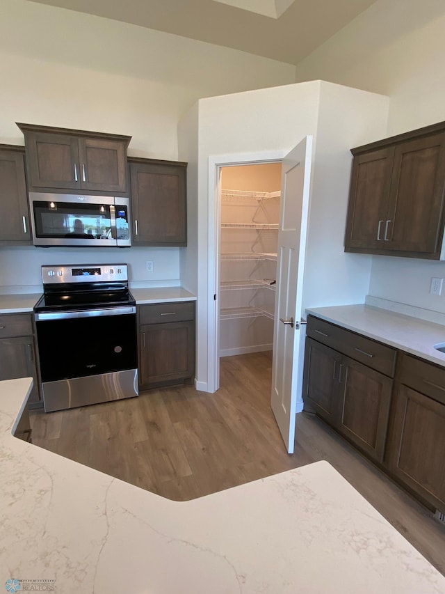 kitchen featuring dark brown cabinets, stainless steel appliances, light wood-style flooring, and light stone counters