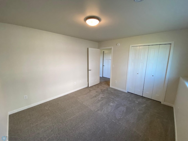 unfurnished bedroom with baseboards, dark colored carpet, and a closet