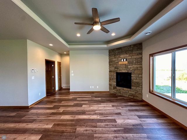 unfurnished living room featuring dark wood-type flooring, ceiling fan, a raised ceiling, and a stone fireplace