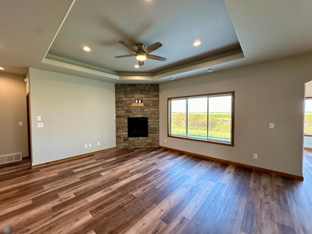 unfurnished living room featuring a fireplace, a raised ceiling, wood-type flooring, and ceiling fan