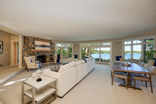 living room featuring a water view, light colored carpet, and a stone fireplace