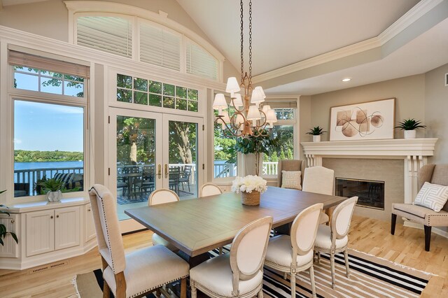 dining space with light hardwood / wood-style floors, a water view, a fireplace, crown molding, and an inviting chandelier