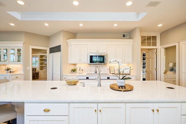 kitchen featuring an island with sink, white cabinetry, light stone countertops, a kitchen bar, and decorative backsplash