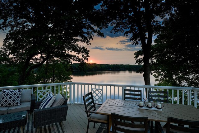 deck at dusk with outdoor lounge area and a water view