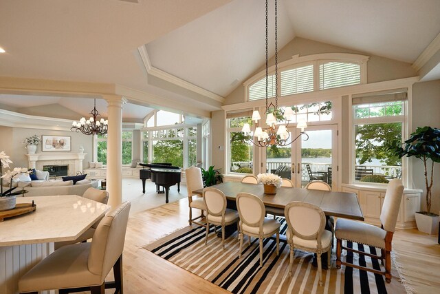 dining room with a notable chandelier, light wood-type flooring, ornate columns, and a water view