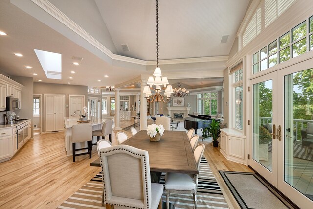 dining space with high vaulted ceiling, light wood-type flooring, crown molding, an inviting chandelier, and a skylight