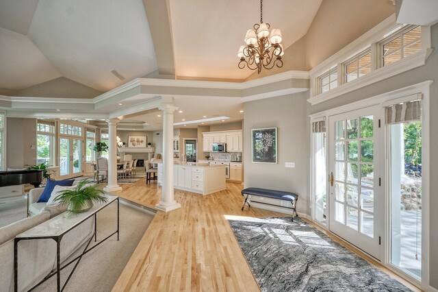 living room with a notable chandelier, light wood-type flooring, decorative columns, and a healthy amount of sunlight