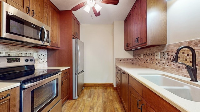 kitchen with sink, a textured ceiling, light wood-type flooring, appliances with stainless steel finishes, and backsplash