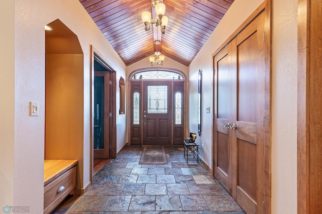 entrance foyer with a chandelier, lofted ceiling, wood ceiling, baseboards, and stone finish floor