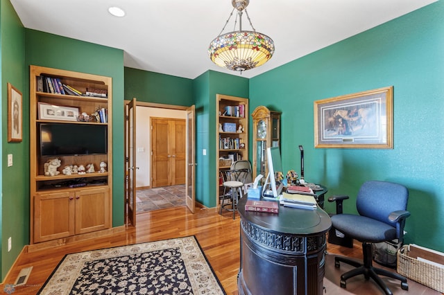 office area with light wood-style floors, built in shelves, and baseboards