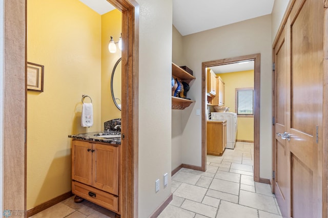 hall featuring washer / clothes dryer, a sink, stone tile flooring, and baseboards