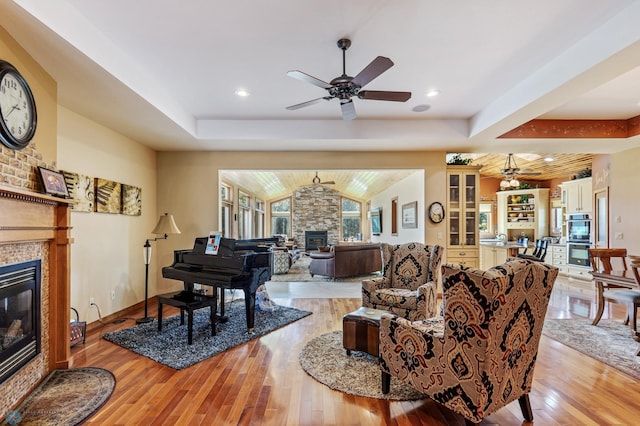 living area with light wood-type flooring, a tray ceiling, a ceiling fan, and a glass covered fireplace