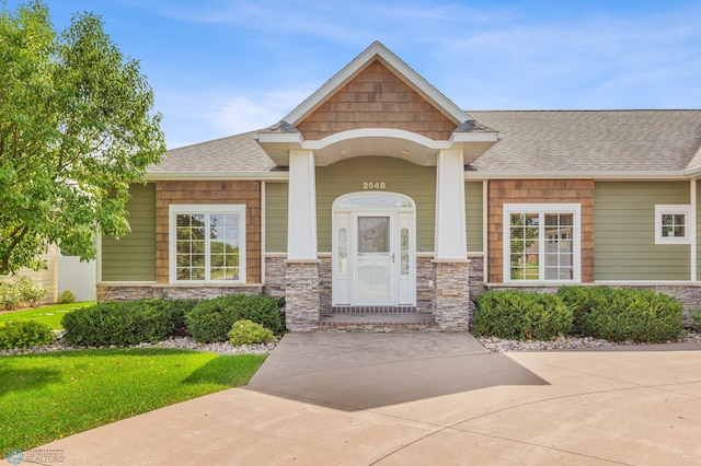property entrance with a shingled roof, stone siding, and a lawn